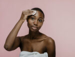 Black woman wiping her face with a cotton pad