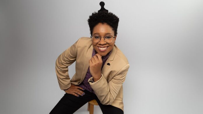 Gautier Lee é uma mulher negra de cabelos curtos, Está sentada com uma mão no queixo. Usa blazer bege.
