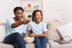 mulher-africana-e-garota-assistindo-tv-com-lanche-mãe-filha-feliz-família-negra-filme-de-cartoons-ou-futebol-pipoca-copiar-168627286