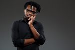 Young successful african businessman in glasses posing over dark background.