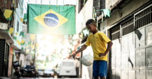 Rua decorada com bandeira do Brasil e menino jogando bola.
