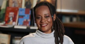 Escritora Eliana Alves Cruz sorrindo com um cenário de livros atrás.