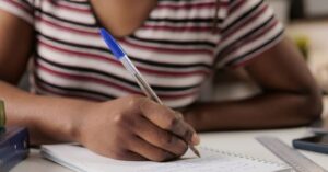 Estudante negra escrevendo no caderno com uma caneta.