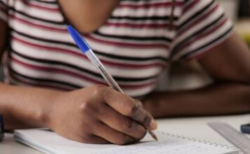 Educação básica e raça: Onde estamos e o que falta para alcançar a verdadeira equidade? Estudante negra escrevendo no caderno com uma caneta.