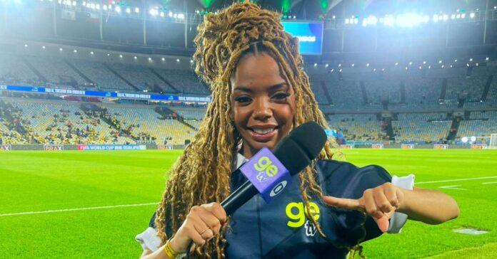 Jornalista negra Jordana Araújo sorri segurando microfone em estúdio de TV.
