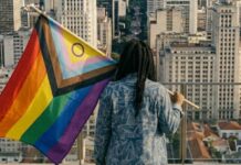 Dia do Orgulho: sem negros e trans, a diversidade vira privilégio branco Mulher negra trans segurando uma bandeira LGBTPIAPN+.
