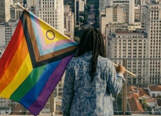 Dia do Orgulho: sem negros e trans, a diversidade vira privilégio branco Mulher negra trans segurando uma bandeira LGBTPIAPN+.